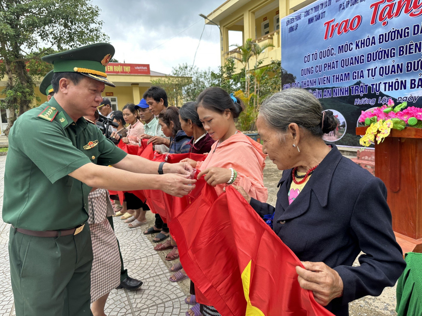 Đại tá Đinh Xuân Hùng (bìa trái) trao tặng cờ Tổ quốc, móc khóa đường dây nóng cho người dân biên giới. - Ảnh: T.L